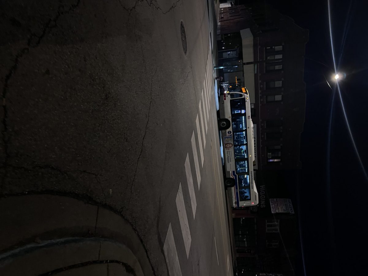 Photograph taken across the street from a bus stopped at a crosswalk at night