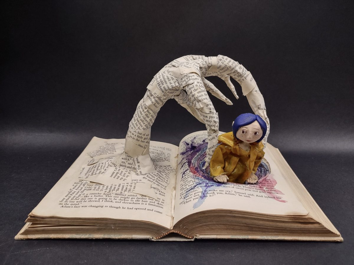 Mixed media sculpture of hand pulling blue haired doll out of other page