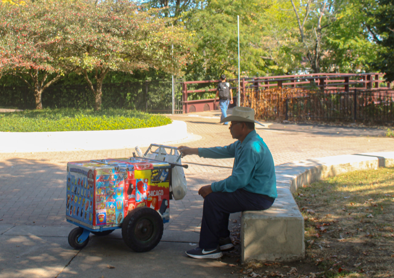 Digital Image of Person sitting on concrete block in park with refrigerated cart in front of him