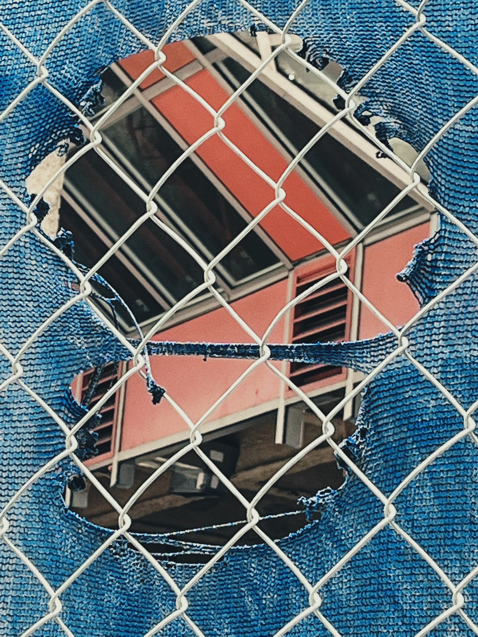 Mixed media collage of building showing under hole in denim fabric with fence pattern over the top