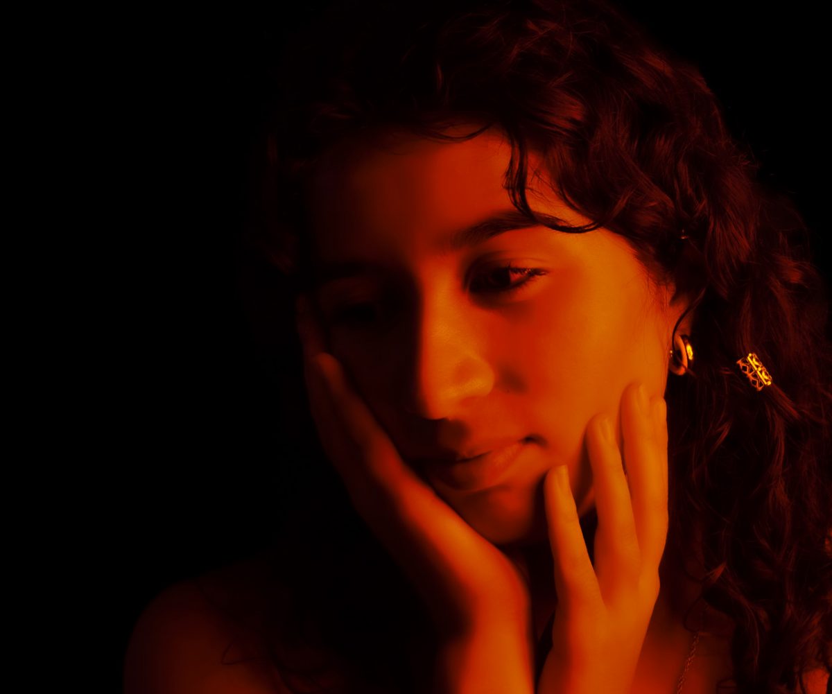 close up photograph of person with dark hair, with both hands under chin with orange glow