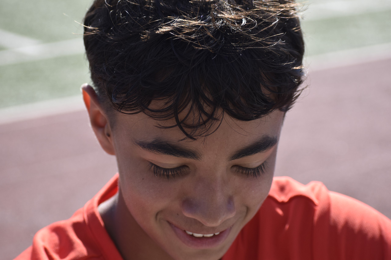 Close-up Photograph of person with dark hair looking down smiling in orange shirt