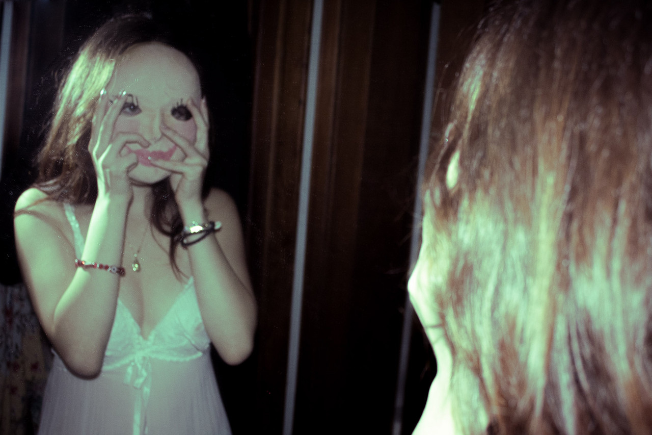 Photograph of person wearing lace top holding mask in front of face in the mirror