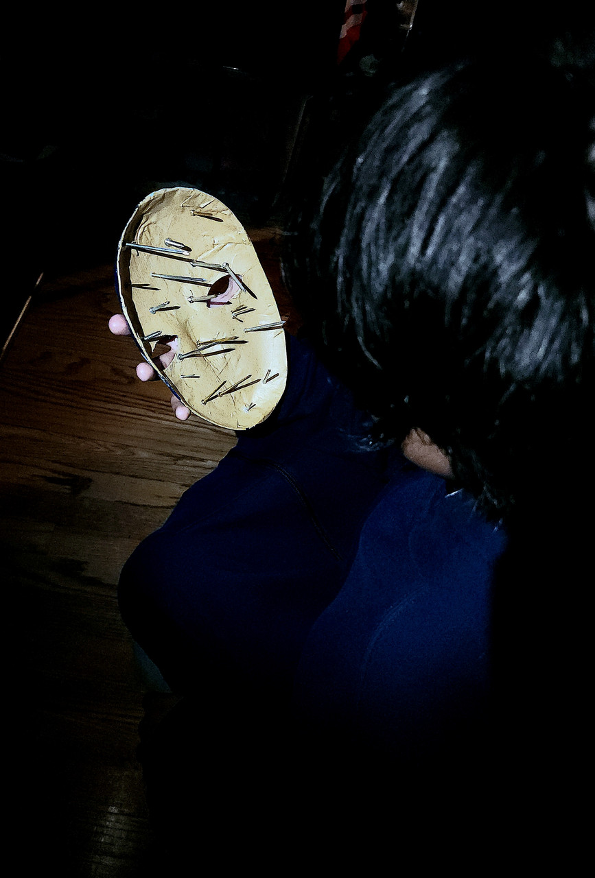 Photograph over a persons shoulder holding a mask with spikes sticking out