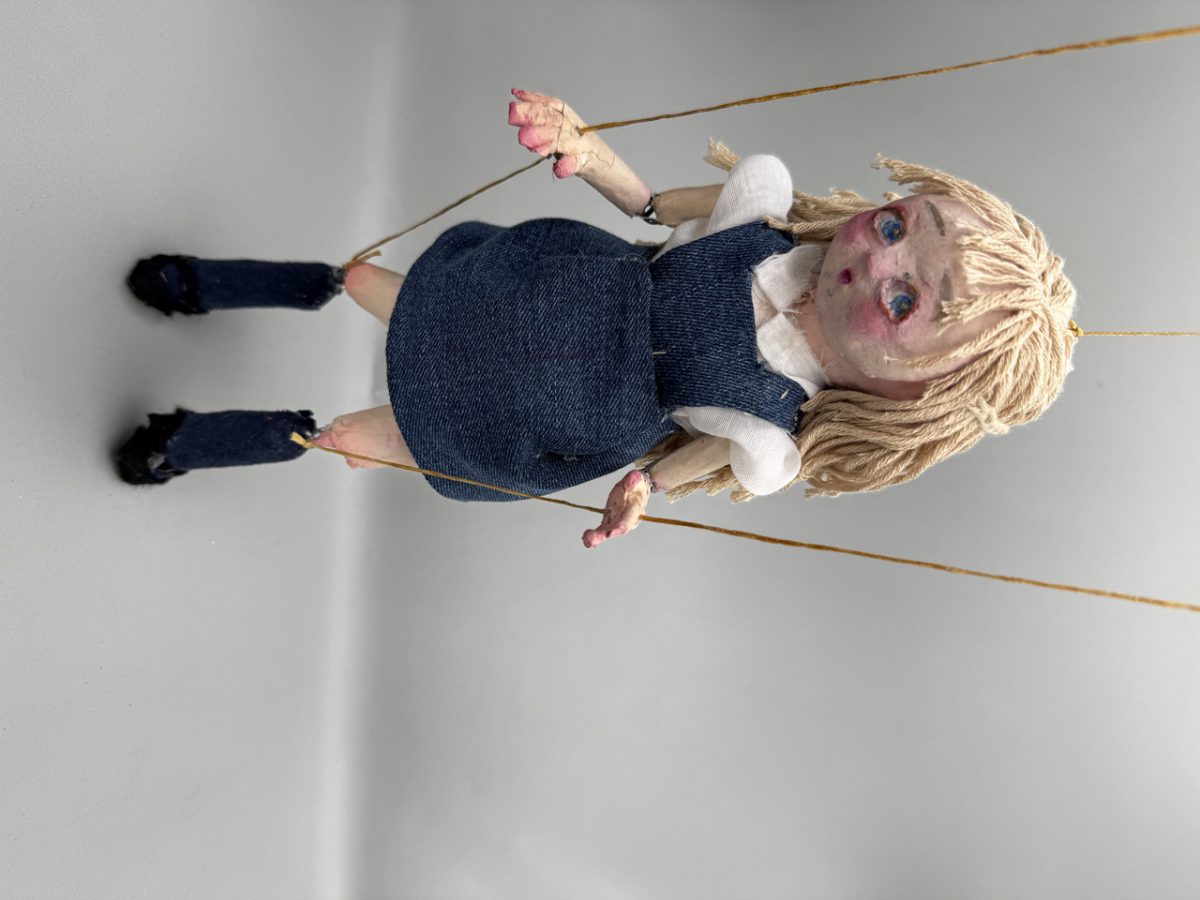 Marionette doll of person with long blonde hair wearing a blue dress with white sleeves and collar