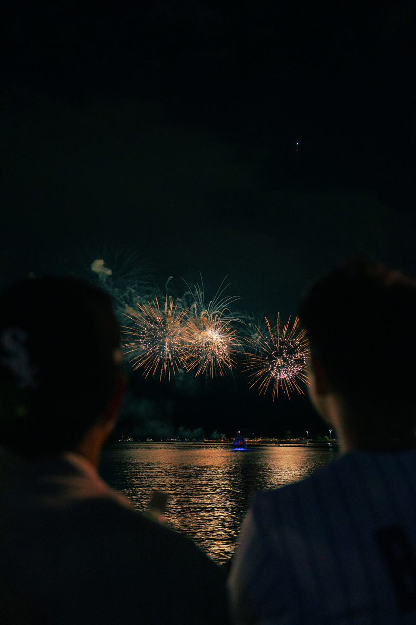 Photograph of two people with multi-colored fireworks going off in background