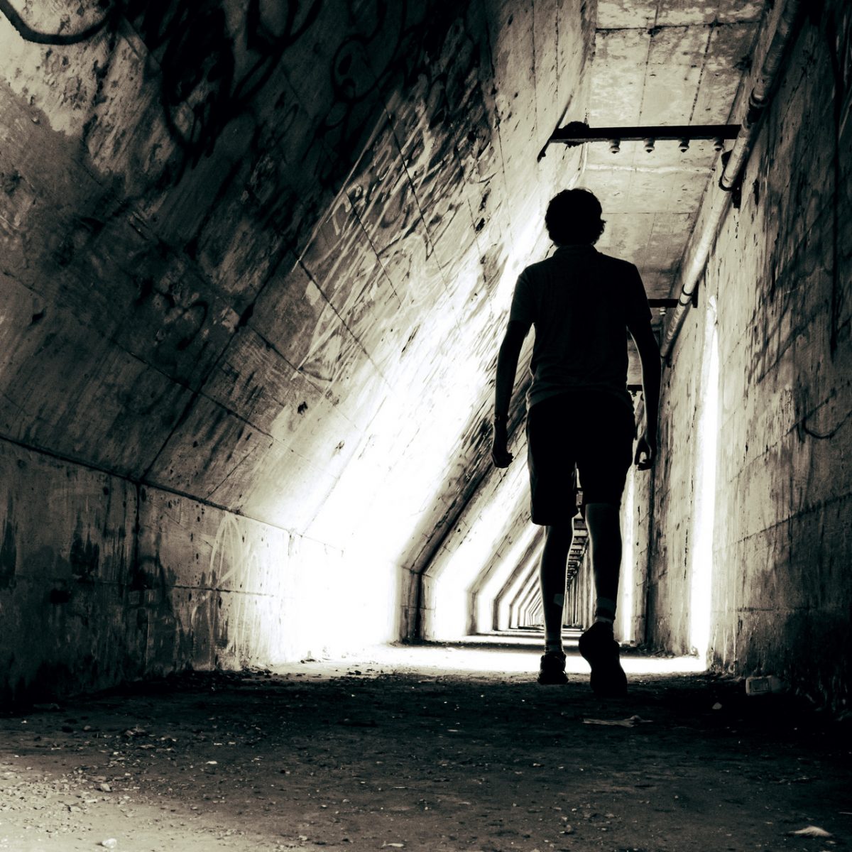 black and white image of silhouette of someone walking down tunnel