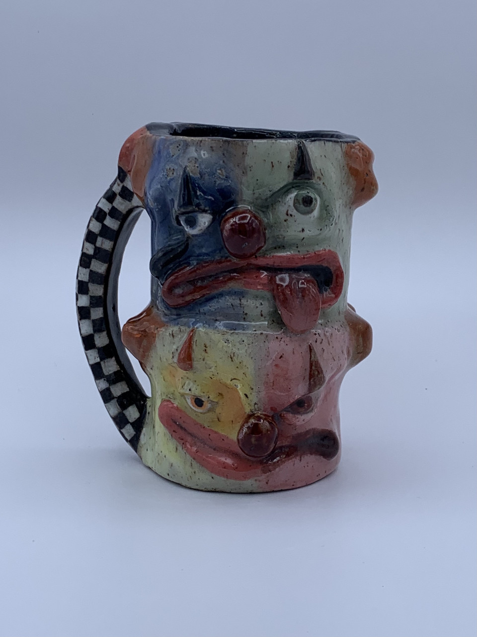 Clay sculpture cup with checkerboard handle and body made of two faces resembling clowns