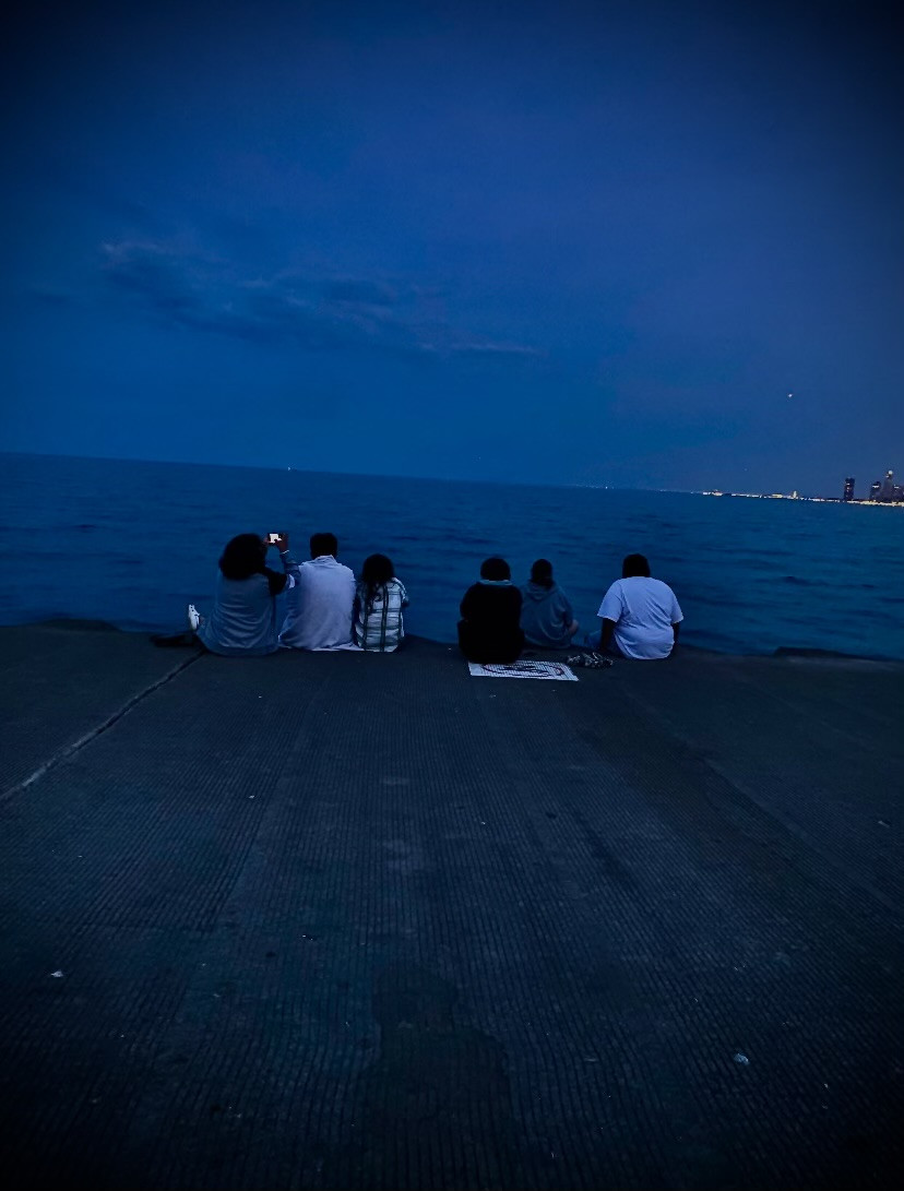 blue based photograph with vignette effect of six people sitting on edge of concrete ledge facing lake and city