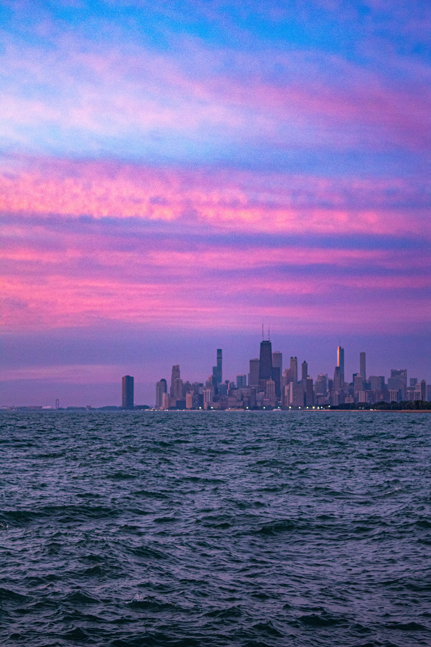 Photograph taken from the lake facing the city with purple pink and blue sky above skyline