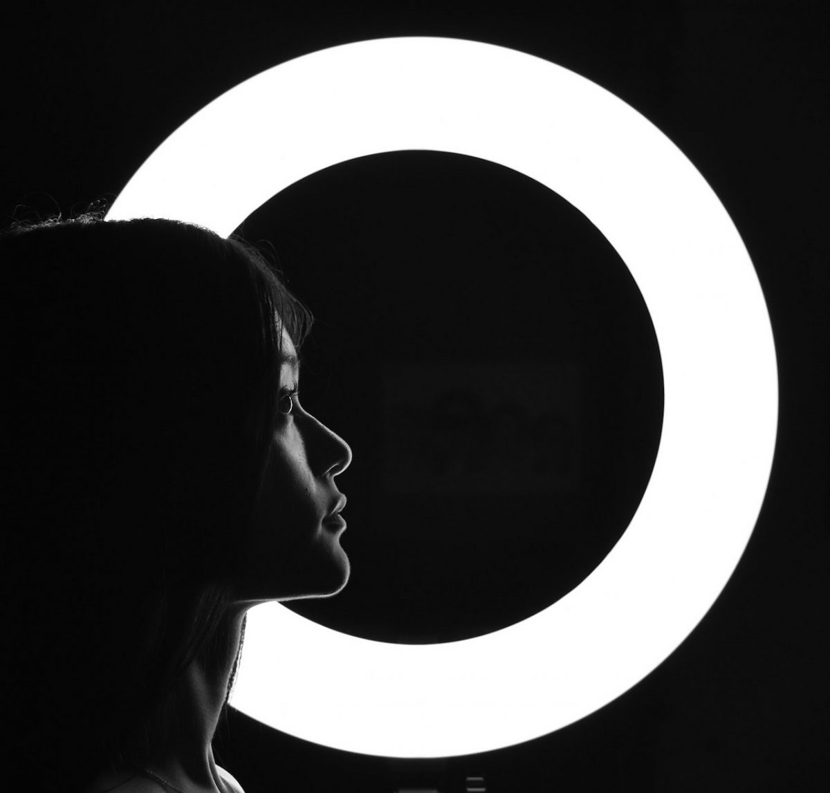 black and white high contrast photo of side of persons face backlit by large ring light