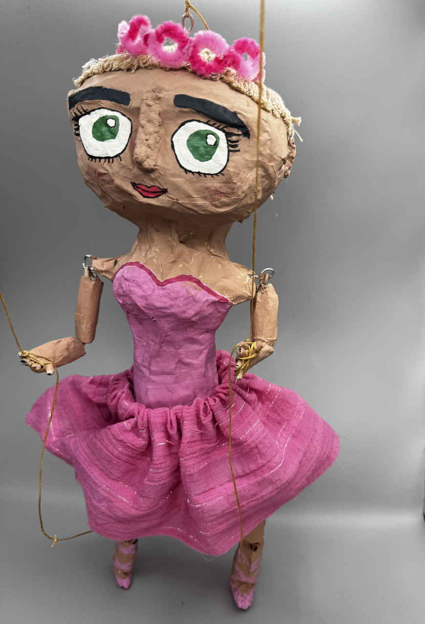 Marionette Doll sculpture of person in pink dress, crown, and pink shoes.