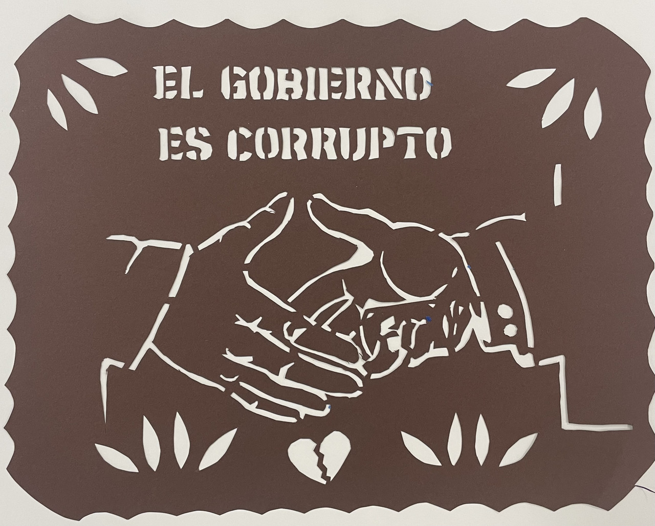 Brown papercut with words el Gobierno es Corrupto, and two shaking hands cut out