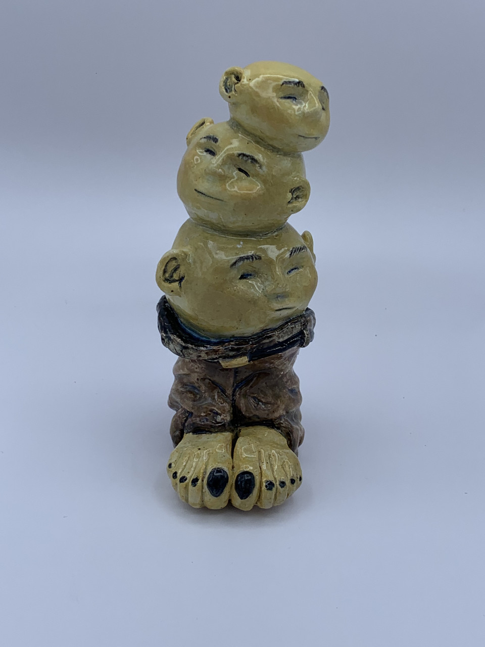 Ceramic sculpture of three heads in pair of brown pants with feet and toes with black nail polish