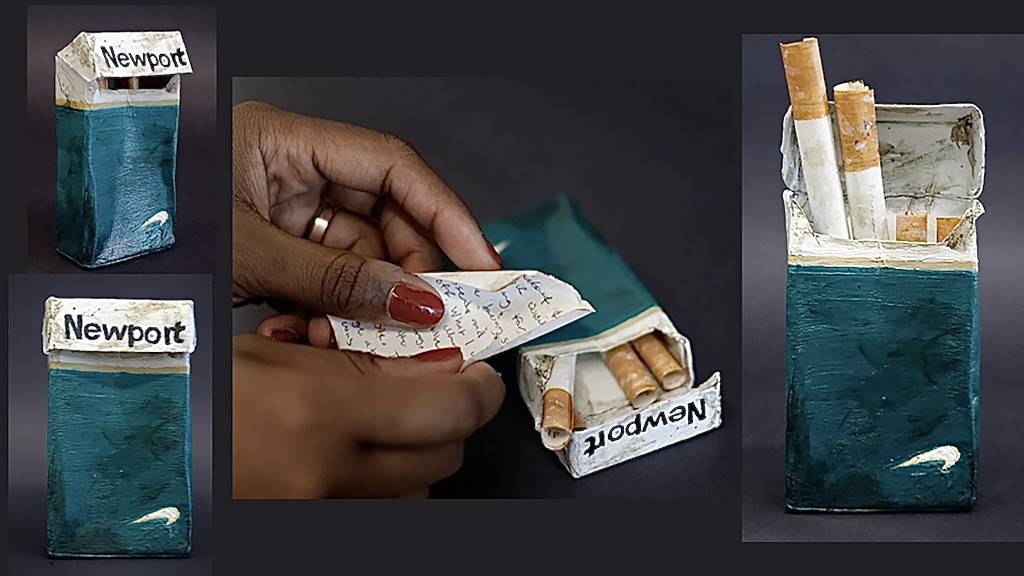 mixed media sculpture of cigarette box and small cigarettes made of paper with messages written inside