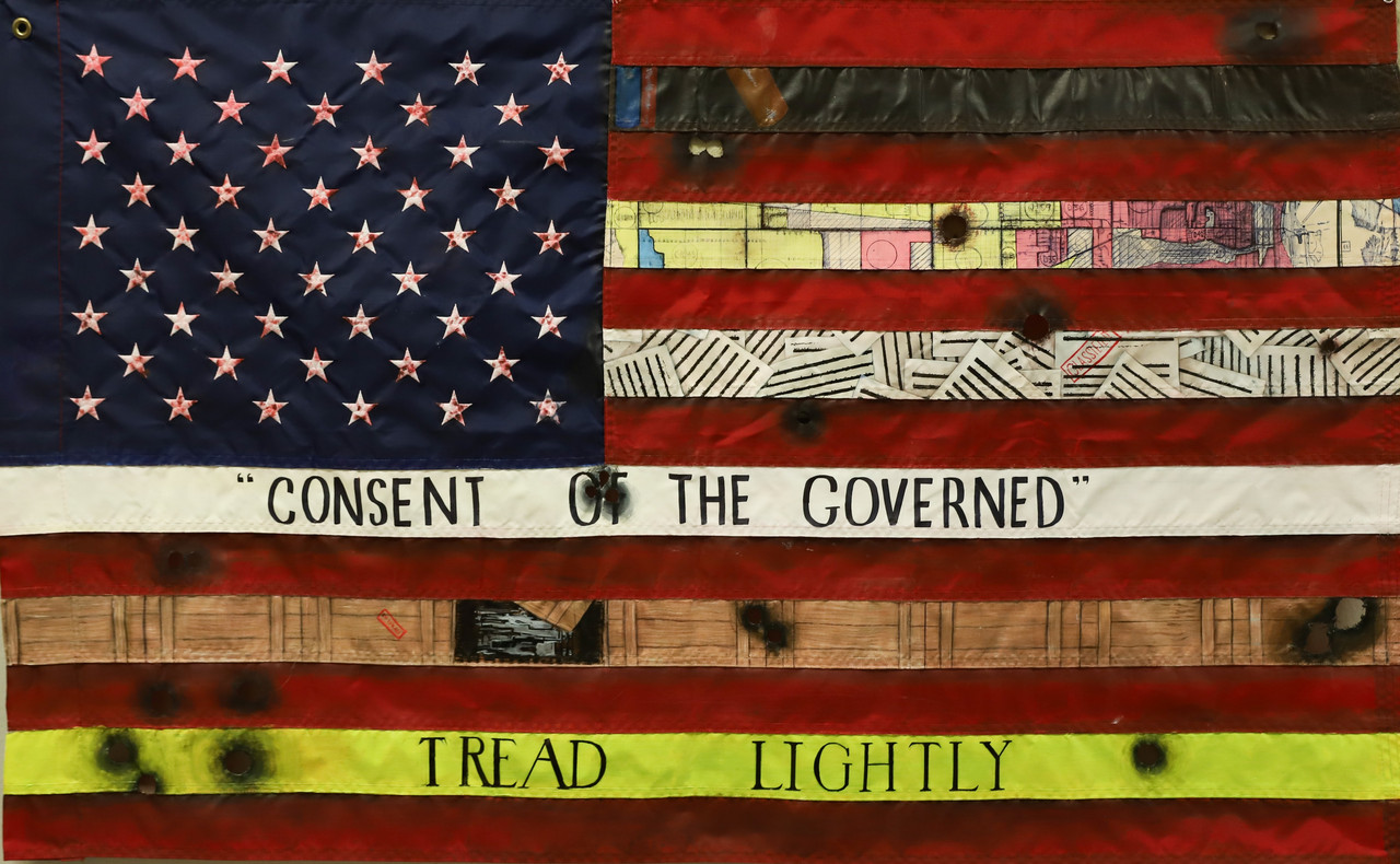 Mixed media art of american flag with altered portions showing different patterns and phrases, burns, and bullet holes, including text "Tread Lightly" and "Consent of the Governed"