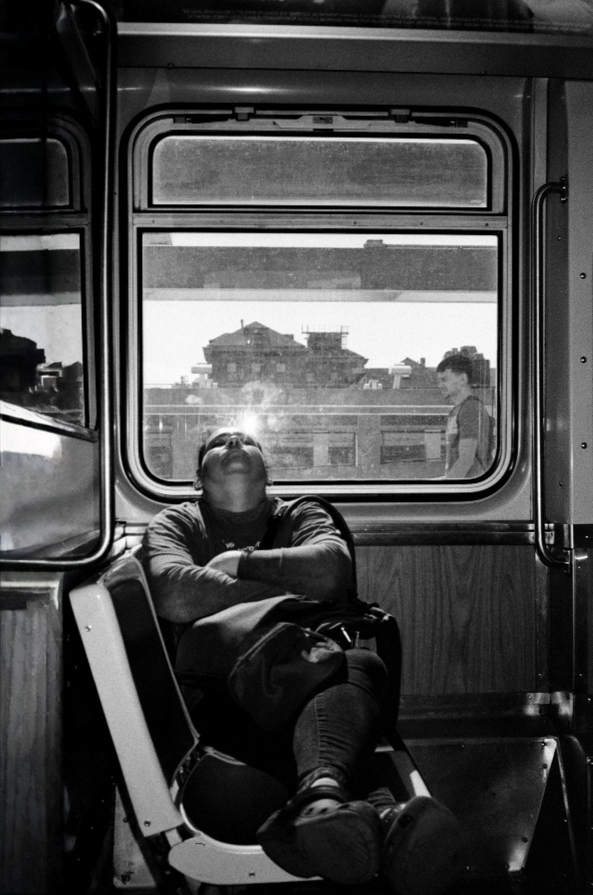 black and white photograph of person sleeping with head back on train